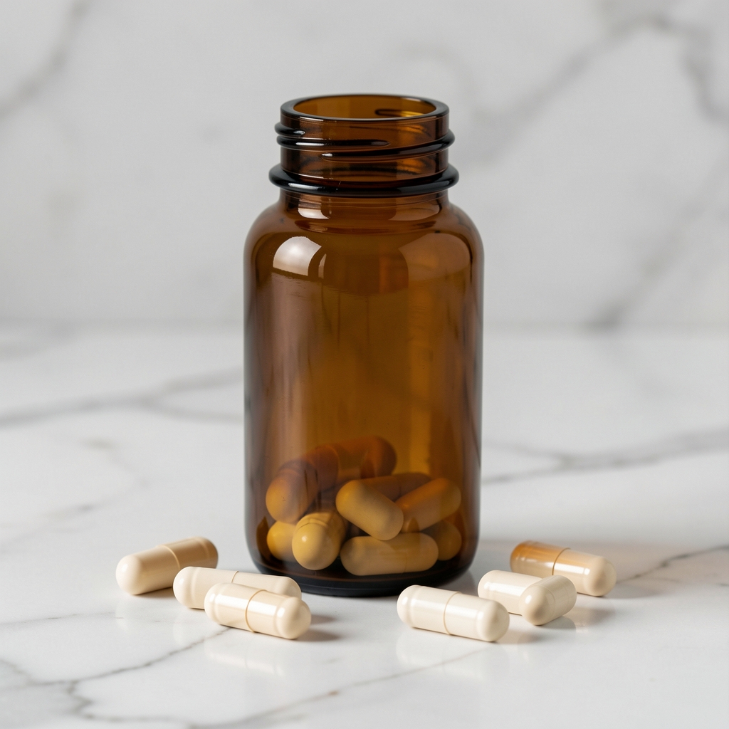 Brown glass vitamin supplement bottle standing on a white marble surface next to scattered capsules in neutral editorial composition
